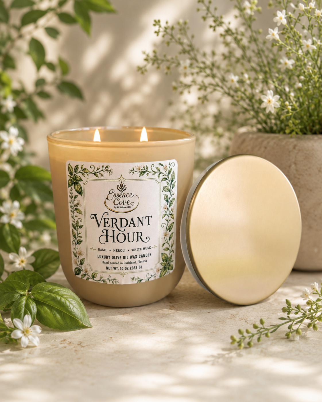 Essence Cove Verdant Hour 10 oz olive oil wax candle with double wick and gold lid surrounded by fresh basil and white flowers.