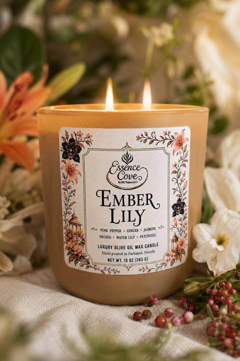 Essence Cove Ember Lily 10 oz luxury olive oil wax candle with double cotton wicks and gold lid lit on a stone surface surrounded by lilies and orchids.