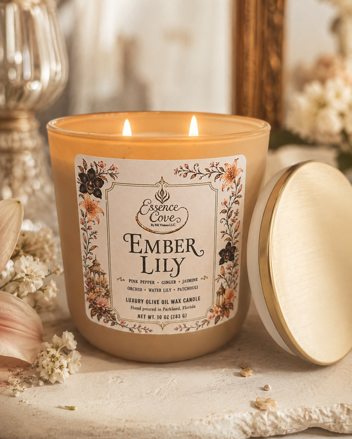 Essence Cove Ember Lily 10 oz luxury olive oil wax candle with double cotton wicks and gold lid lit on a stone surface surrounded by lilies and orchids.