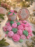 Blush Botanica floral-themed wax melts shaped like pink roses and green leaves scattered around an eco-friendly product container by Essence Cove.